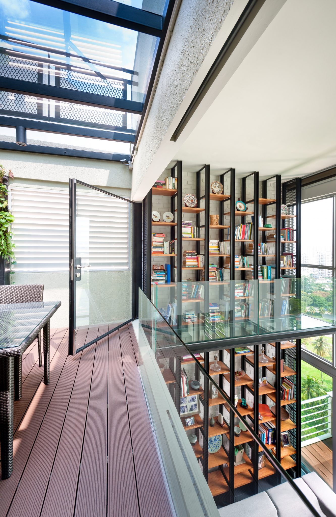 Balestier Penthouse double-height library: black steel shelving against white brick with a glass walkway above