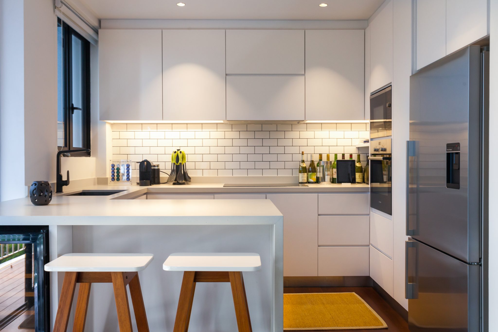 Cavenagh House by PIU: white kitchen with subway tiles, timber stools and under-cabinet lighting