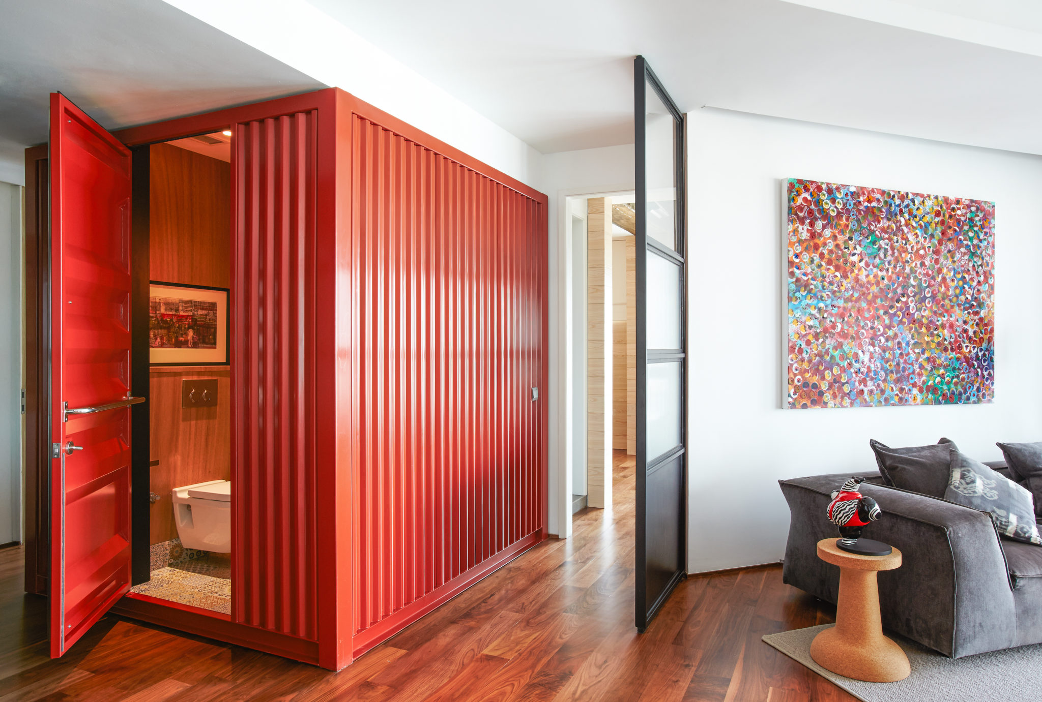 The Regalia by PIU: red corrugated steel container room with an open red door, set inside a white apartment